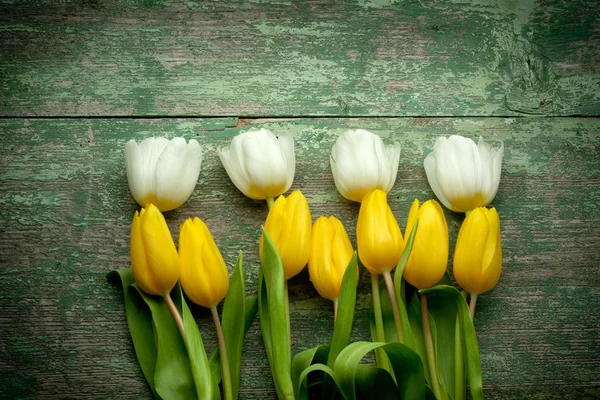 Kopott, fából készült asztal fölé fehér és sárga tulipánok — Stock Fotó