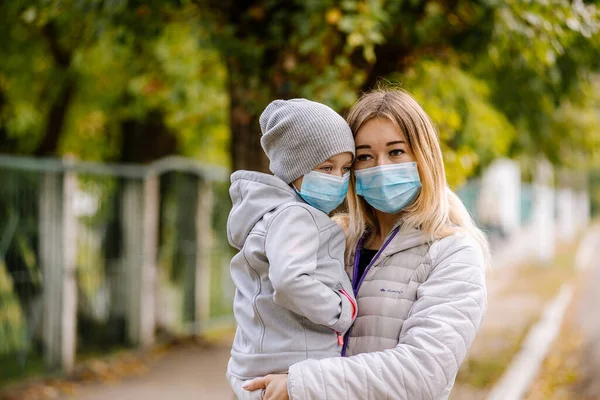 Uma menina com uma criança está de pé na estrada em uma máscara médica protetora. pandemia de coronavírus, Covid 19 — Fotografia de Stock