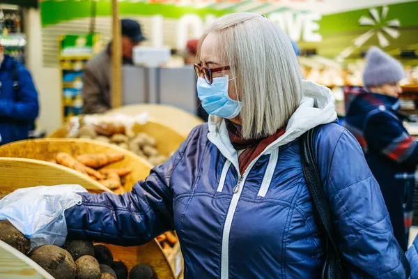 Старуха в медицинских масках закупается в супермаркете в поисках еды — стоковое фото