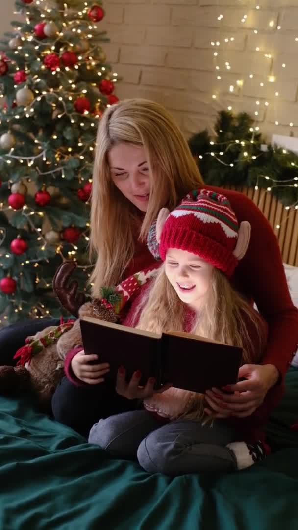 Mother and daughter reading fairytales during Christmas eve, wonderful atmosphere of love and trust, belief in miracles, happy holidays. Vertical video — Stock Video