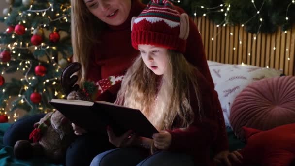 Mor och dotter läser sagor under julafton, underbar atmosfär av kärlek och tillit, tro på mirakel, glada högtider — Stockvideo