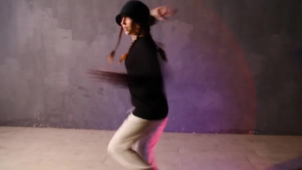 Coreografia da dança moderna. Jovem engraçada em um chapéu dança hip hop, estilo livre no salão de dança sob uma luz de estúdio colorida piscando. Tiro do ponto de vista. — Vídeo de Stock