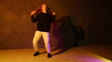 Modern dansın koreografisi. Uzun saçlı, hip hop yapan, dans salonunda serbest dans eden parlak stüdyo ışıkları altında dans eden komik bir genç kadın. Bakış açısından ateş edilmiş..