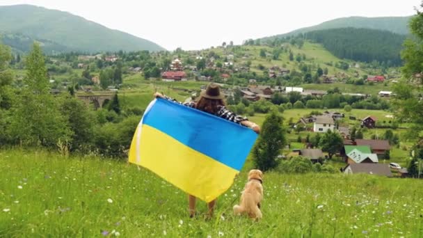 Een meisje met een vlaggetjeshond zwaait met de Oekraïense vlag tegen de achtergrond van bergen. Onafhankelijk van Oekraïne. — Stockvideo