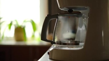 Sabah kahvesi. Demlenmiş kahve damlaları yavaşça beyaz kahve makinesinin platformuna monte edilmiş kahve demliğine damlıyor..