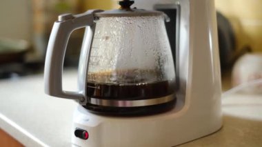 Sabah kahvesi. Demlenmiş kahve damlaları yavaşça beyaz kahve makinesinin platformuna monte edilmiş kahve demliğine damlıyor..