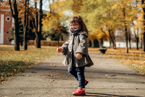 おしゃれなコートを着た幸せなかわいい女の子とスタイリッシュな眼鏡を歩くと笑い 子供は暖かい秋の公園 幸せな子供時代を楽しんでいます — ストック写真