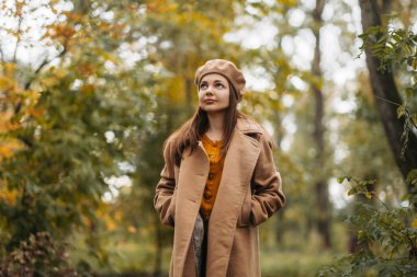 Yünlü ceketli bir kız güzel bir sonbahar parkında yürüyor..