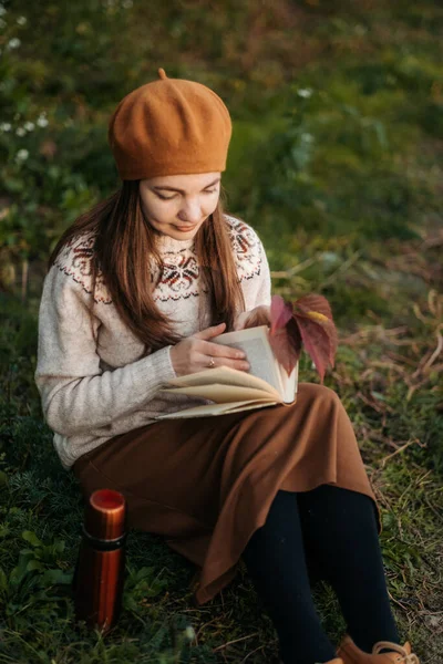 一个穿着法国贝雷帽的女人的画像 一个穿着针织毛衣和棕色贝雷帽的年轻而坦率的女人正坐在草地上看书 法国女孩 千年一代 — 图库照片