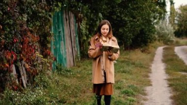 Yünlü paltolu romantik bir kız köyde bir kitapla yürüyor.