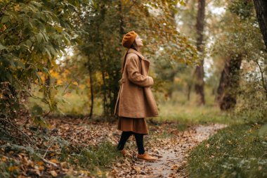 Yünlü ceketli bir kız güzel bir sonbahar parkında yürüyor..