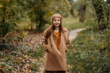 Yünlü ceketli bir kız güzel bir sonbahar parkında yürüyor..