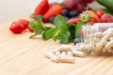 Viitamins supplements in the glass bottle on the wooden table with variety fruit.