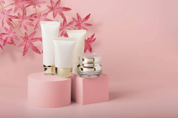 Cosmetics packaging - Set of different cosmetic empty tubes of cream and serum jar  on product stands. Beauty, studio shot. Unbranded blank packages on pink background