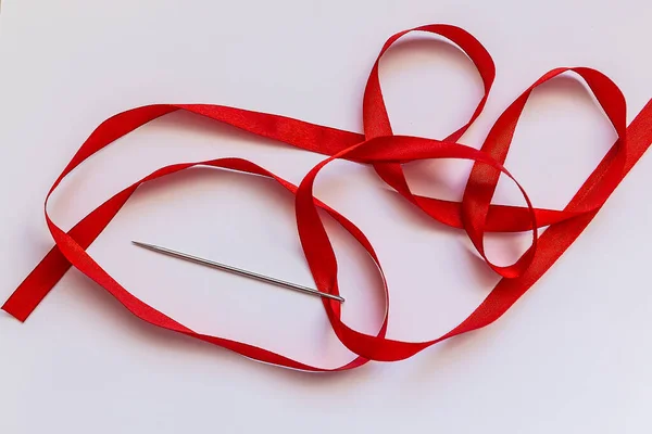 Needle with red thread. Red ribbon. Sewing