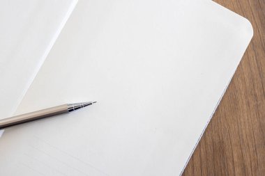 Ofisteki ahşap masa zemininde boş defter sayfası ve kalemin üst görünümü. 