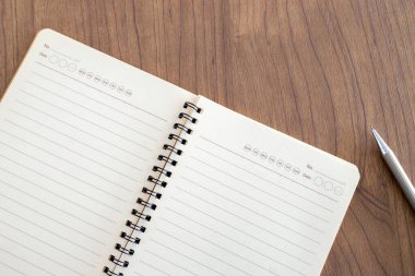 Ofisteki ahşap masa arka planındaki boş defter sayfası ve kalemin üst görüntüsü. Metin için boşluk. düz yat