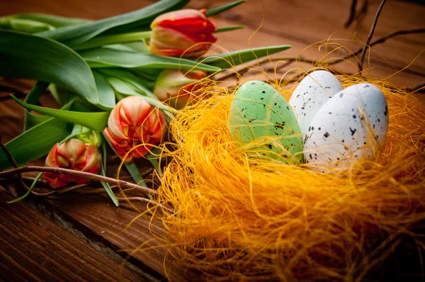 Vogeleier im Nest mit Tulpenblüten auf altem hölzernem Hintergrund — Stockfoto