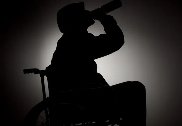 Sad man sitting on wheelchair in empty room and drinking alcohol — Stock Photo, Image