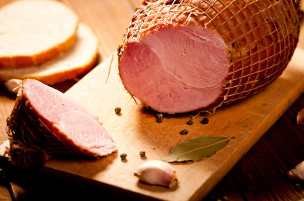 Whole ham with bread in the background, selective focus