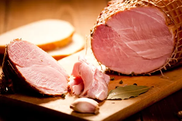 Prosciutto intero con pane sullo sfondo, messa a fuoco selettiva — Foto Stock