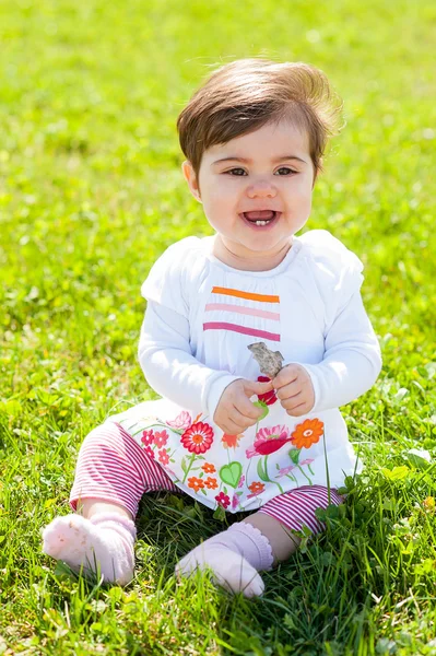 Sonriente bebé sentarse en la hierba con una hoja en las manos — Foto de Stock