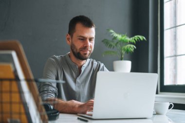 Cadual Gri uzun kollu gülümseyen genç iş adamı karanlık modern ofis odasında dizüstü bilgisayarda çalışıyor.