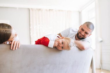 Genç ve mutlu bir aile aydınlık oturma odasında yatakta. Kız bebeğe aşık bir adam ve bir kadın gülümseyip kameraya bakar. Evdeki ortak eğlence.