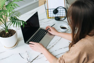 Top view of business woman on working place with cup of coffee, notes and open laptop on white marble table in the bright modern office 