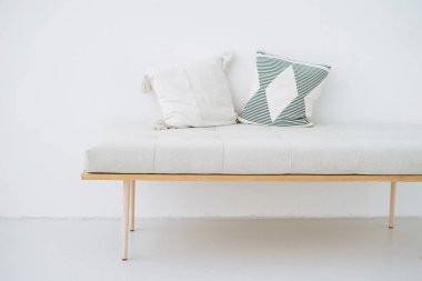 Minimalist ahşap bankta beyaz bir duvar arkasında eko tarzı yastıklar var.