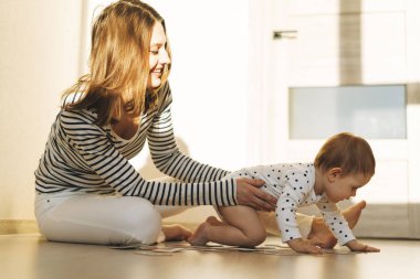 Mutlu bir anne, genç bir kadın ve küçük bir kız bebek evde ışıkla eğleniyorlar.