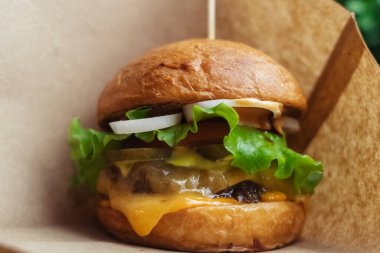 Standart bir hamburgerin yakın çekimi. Restoranda ya da kafede yetişkin fast food 'u. Etli, peynirli ve otlu hamburger malzemelerinin Macro fotoğrafı. Tüm aile için eko-burger.