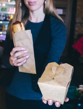 Yemek servisi. Kız elinde hazır yiyeceklerle kese kağıdı tutuyor. Covid 19 'a karşı koyma konsepti. Restorandan ya da kafeden teslimat var. Yemek konteynerleri açılıyor