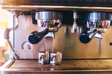 Kahve hazırlayan bir baristanın yakın çekimi. Kahve makinesinde cappuccino yapma süreci. Elde ölçü kabı. Sıcak içecek bir kağıt bardağa doldurulur. Paket yemek.