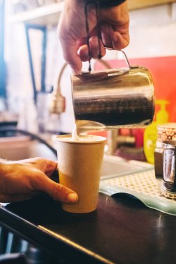 Kahve hazırlayan bir baristanın yakın çekimi. Kahve makinesinde cappuccino yapma süreci. Elde ölçü kabı. Sıcak içecek bir kağıt bardağa doldurulur. Paket yemek.