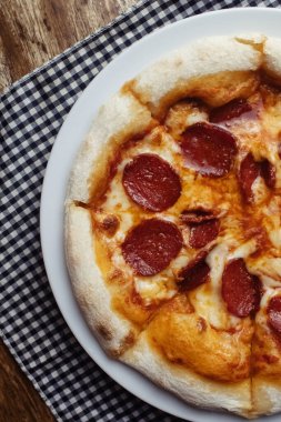 Pepperoni pizza yakın çekim. Sosis halkaları ve otlarla kaplı bir yemek. Restoranlarda ve kafelerde İtalyan mutfağı. Aşçılıktaki et malzemeleri kavramı.