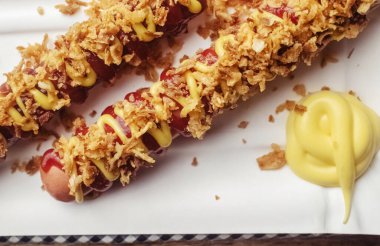 Izgara sosisler yakın plan. Et tabağı kurutulmuş karamelli soğan serpiştirilmiş. Üstünde rendelenmiş peynir, hardal ve ketçap var. Tahta bir arka planda izole edilmiş. Kafelerde ve restoranlarda fast food