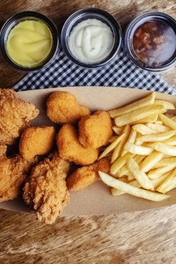 Tavuk nugget, hamurlu kanat ve patates kızartması. Bir karton kutuda üç tabak. Fast food kafeler ve restoranlar. Yemekler sıraya dizildi. Üç çeşit sos.