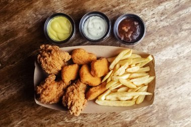 Tavuk nugget, hamurlu kanat ve patates kızartması. Bir karton kutuda üç tabak. Fast food kafeler ve restoranlar. Yemekler sıraya dizildi. Üç çeşit sos.