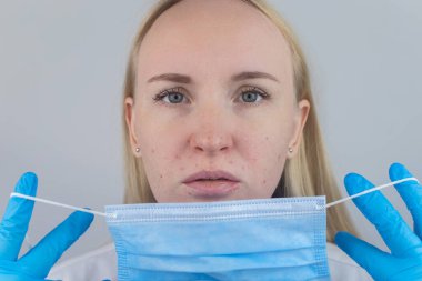 Doktor koruyucu maskeyi çıkarır ve yüz derisinde tahriş gösterir. Antiviral önlemler. Covid 19 'a karşı korunma aracı. Uzun zamandır maske takıyorum. Yüzünde sivilce ve aşınma. Kuru dudaklar ve kırmızı noktalar.