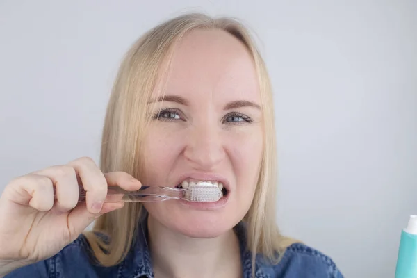 一个正在刷牙的女孩的特写镜头 看着镜子前面 口腔卫生 在清洁口腔的物品的手上 牙刷和牙膏 因白人背景而被隔离 — 图库照片