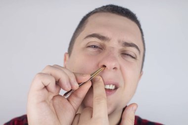 Adam burun kıllarını cımbızla çekiyor. Erkek hijyen ürünlerine yakın çekim. Beyaz arka planda izole edilmiş. Erkek, aynaya bakar gibi ekrana bakar..
