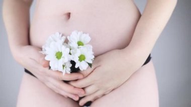 Bir kadın vücuduna yakın çekim. Kadın kasığı. Çiçeklerin öne çıktığı külotlar. Kadın mahrem sağlığı hakkındaki konsept fotoğraf. Erotizmden eser olmayan hassas ve şehvetli bir vücut. Seçici odak.