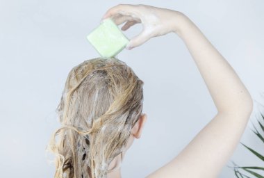 Solid hair shampoo. Close-up of a blonde girl in the bathroom, which lathers her hair with dry shampoo. Lots of foam and peek effect. clipart
