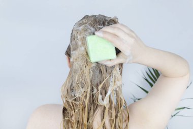 Solid hair shampoo. Close-up of a blonde girl in the bathroom, which lathers her hair with dry shampoo. Lots of foam and peek effect. clipart