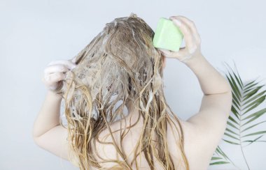 Solid hair shampoo. Close-up of a blonde girl in the bathroom, which lathers her hair with dry shampoo. Lots of foam and peek effect. clipart