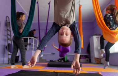 Çocuklar için sinek yogası. Çocuklar ve koç bez tuvaller üzerinde hava akrobasisi yapıyorlar. Ebeveynler ve çocuklar hamaklarda eğitim görüyorlar. Hava jimnastiği.