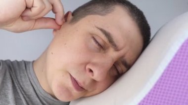 Adam kulak tıkacı takıyor. Turuncu gürültü bariyerine yakın çekim. Derin uykuda. KBB doktoru çevredeki gürültüyü azaltmak için turuncu kulaklık tavsiye ediyor. Seslere karşı hassasiyet artışı.