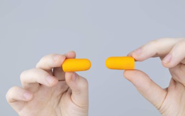 Adam kulak tıkacı takıyor. Turuncu gürültü bariyerine yakın çekim. Derin uykuda. KBB doktoru çevredeki gürültüyü azaltmak için turuncu kulaklık tavsiye ediyor. Seslere karşı hassasiyet artışı.