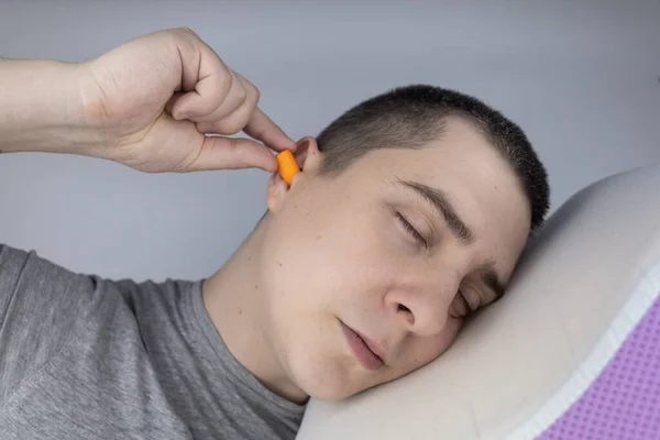 あの男は耳栓をしている オレンジのノイズバリアのクローズアップ 深い眠りだ 耳鼻咽喉科医は 周囲の騒音を減らすためにオレンジの耳痛をお勧めします 音に対する感度の向上 — ストック写真